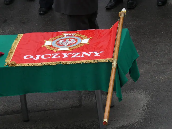 Odznaka Związku OSP RP i złota frędzla; na drzewcu widać pamiątkowe gwoździe.